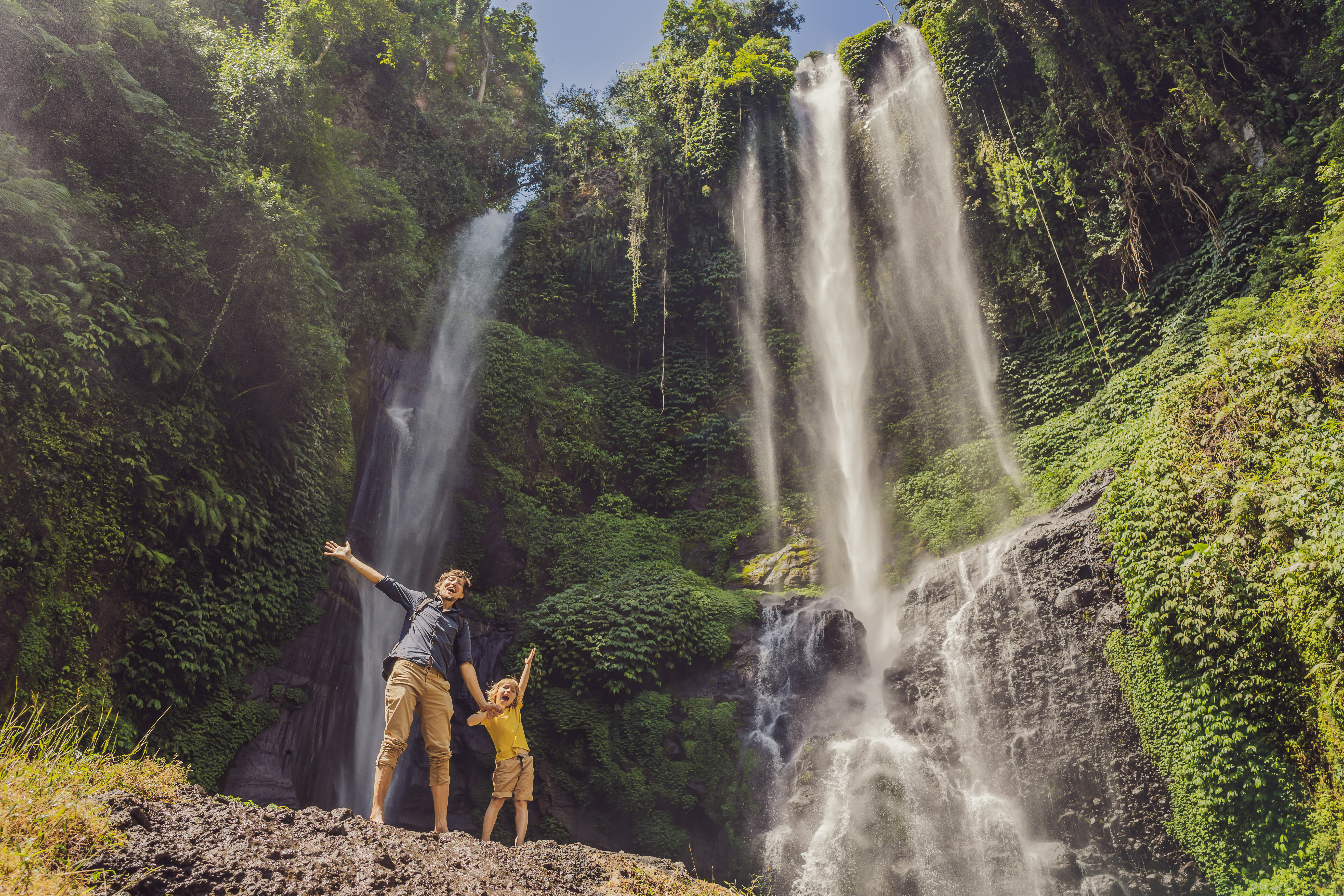 Family enjoying a beautiful waterfall. Parents and children smiling and playing in the refreshing water.