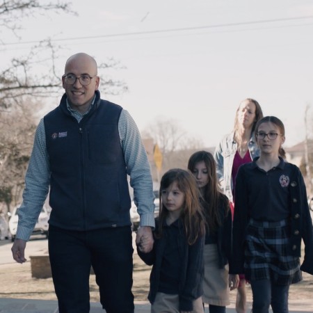 President, KCCF and his family walking down a sidewalk on a sunny day, smiling and holding hands.