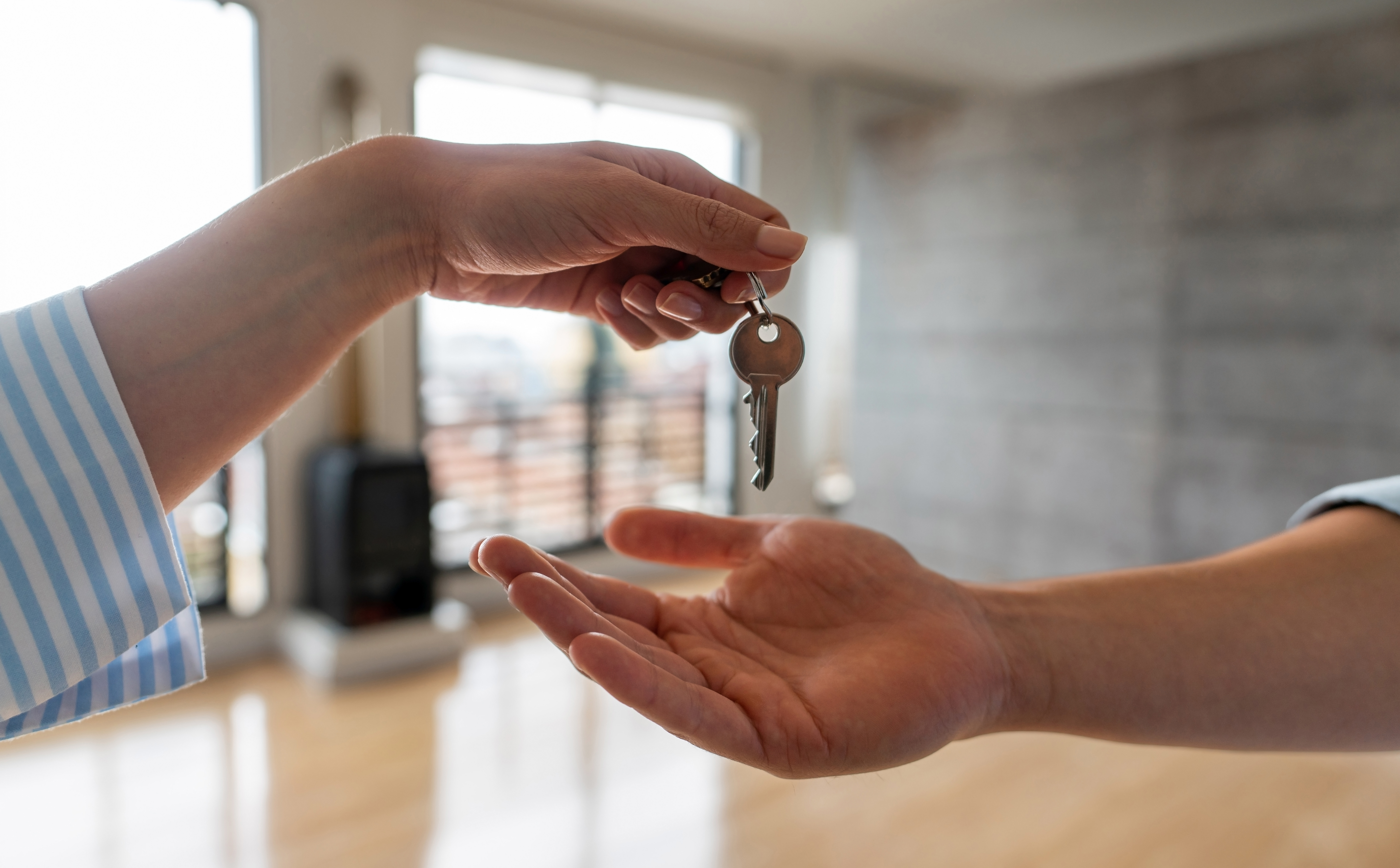 A person handing a key to another person, symbolizing the transfer of ownership or access.