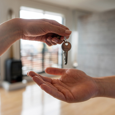 A person handing a key to another person, symbolizing the transfer of ownership or access.