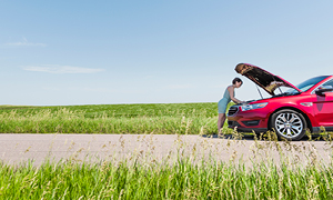 Ženska gleda pod pokrov vozila v motor, ker se ji je avto pokvaril sredi ceste