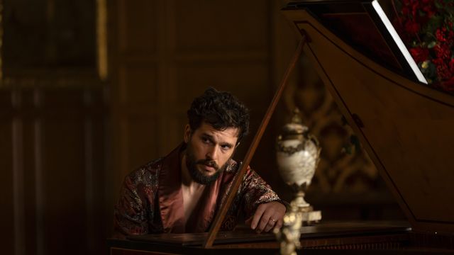 Kit Harington as Sir Henry Muck leans over a piano in an ornate room, looking intense