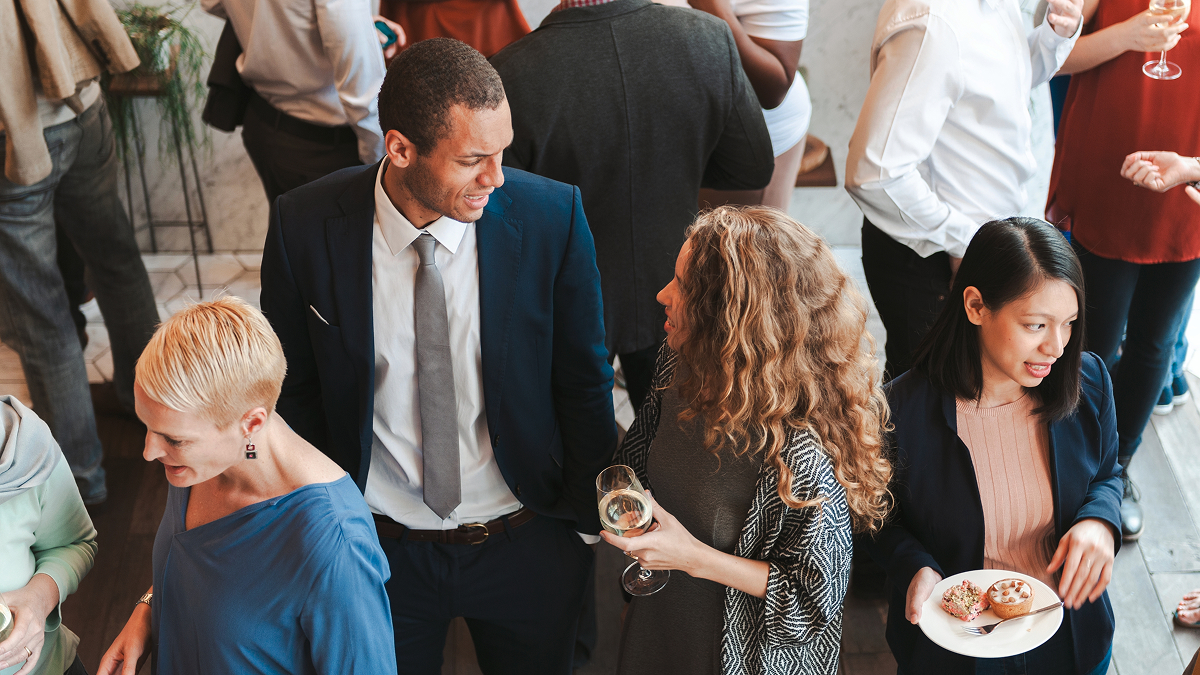 Group of professionals networking at a social event, engaging in conversation and holding drinks and food.