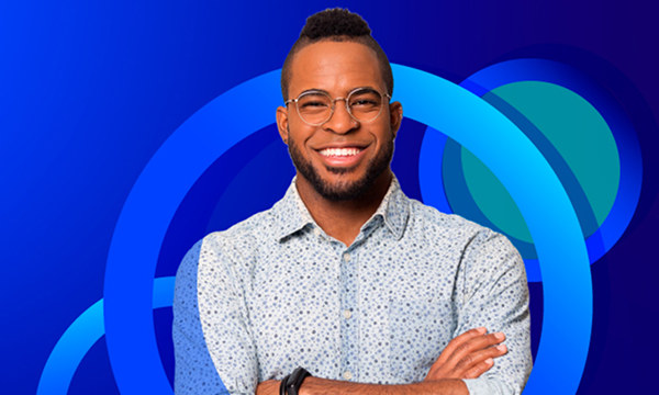 A smiling man with glasses, a patterned button-down shirt, and a stylish haircut stands with his arms crossed. The background is a vibrant blue with concentric blue circular patterns.