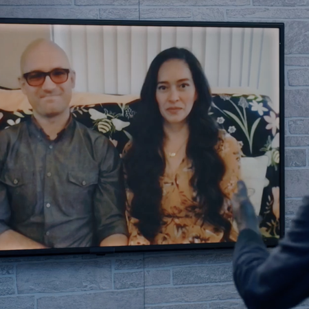 Husband and wife appear on a television screen while being interviewed by a man