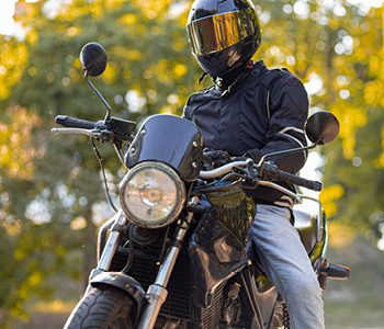 Motorist v temni moto-opremi in s črno integralno čelado sedi na motorju.