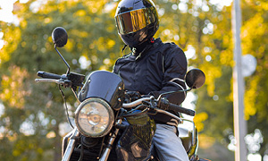 Motorist v temni moto-opremi in s črno integralno čelado sedi na motorju.