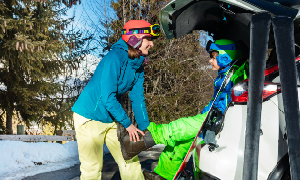Mama pomaga sinu pri obuvanju pancerjev za smučanje po tem, ko so se na smučanje z avtomobilom pripeljali zgodaj zjutraj.
