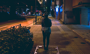 Ženska na ulici ponoči je v temnih oblačilih celo pod uličnimi svetilkami slabo vidna