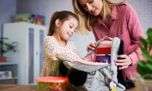 Mama hčerki pomaga v šolski nahrbtnik pospraviti šolske potrebščine.