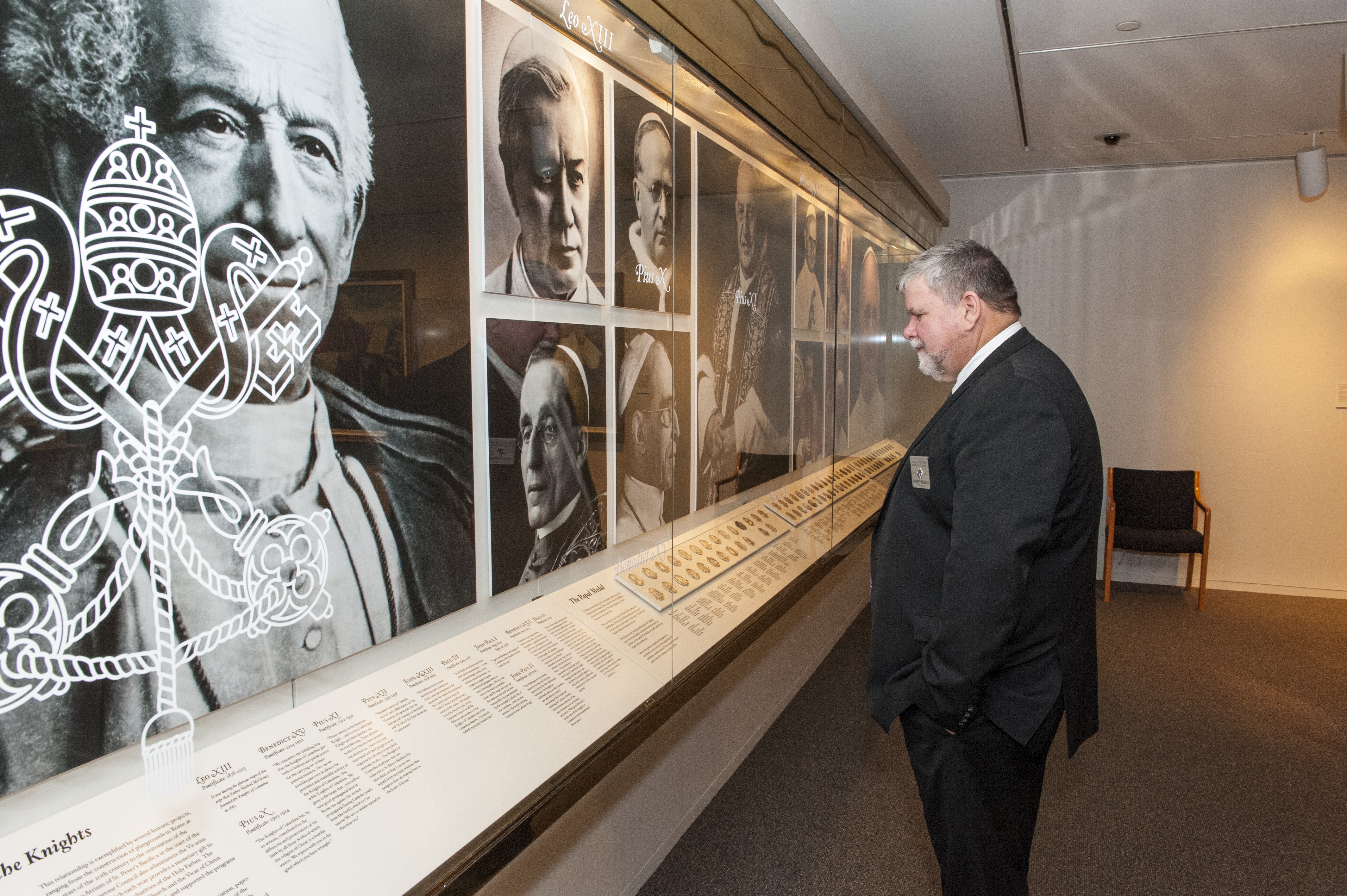 Photo of the Papal Gallery with a man in a suit looking at a case of papal medals.