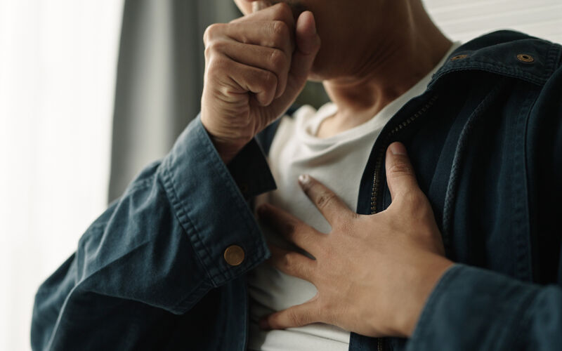 photo of person coughing with one hand over his mouth and another on his chest