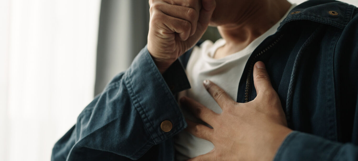 photo of person coughing with one hand over his mouth and another on his chest