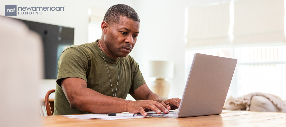 A man in a military t-shirt typing on a laptop.