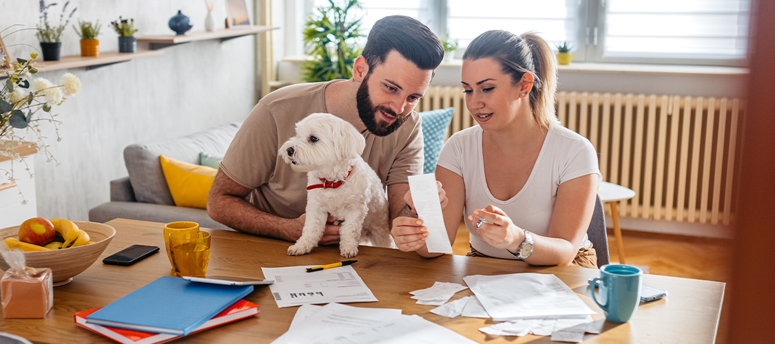 A couple with a dog between them sitting at a table going over paperwork.