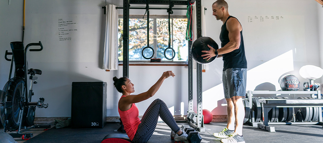 A man handing a woman sitting up on a mat a weighted ball.