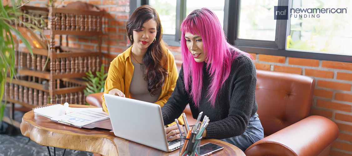 A trans person and their partner sitting on a chair in front of a laptop.