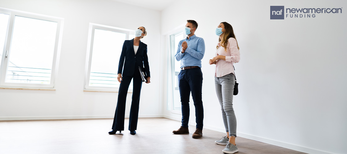 A couple and a real estate agent in an empty room. Everyone's wearing masks.