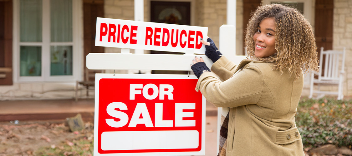 A woman putting a price reduced sign on a home for sale sign