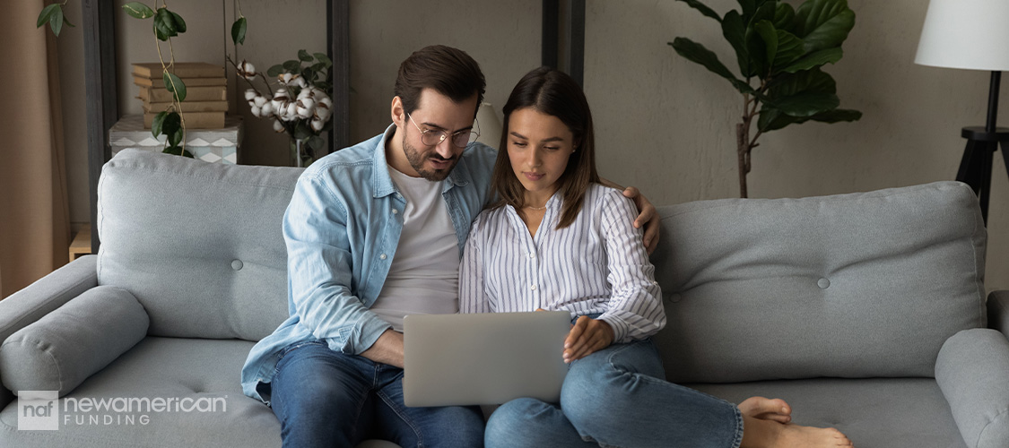 A couple sitting on a couch looking at a computer.
