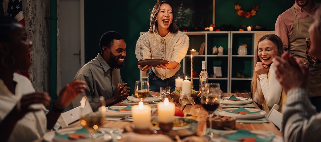A group of friends smiling and laughing around a table lit with candles.