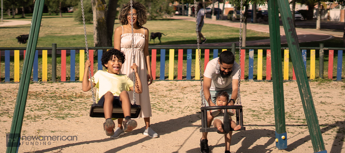 A family pushing kids on swings at a park.