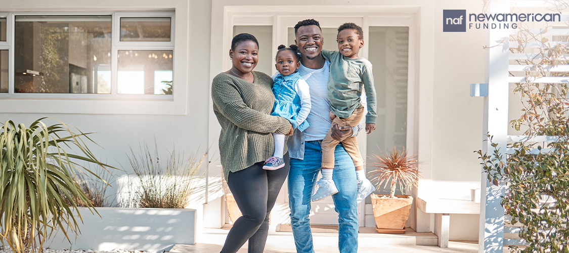 A couple standing in front of a home with two kids in their arms.