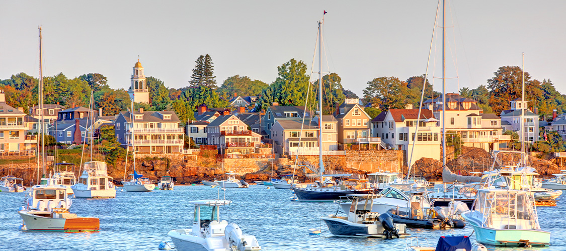 A coastal photo of Massachusetts with boats on the water and homes in the background.