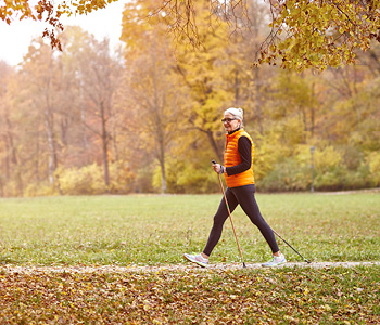 Starejša gospa na sliki v parku jeseni s palicami izvaja nordijsko hojo.
