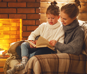 Mama s hčerko v naročju prebira pravljice ob kaminu - nevarnost CO2 so preprečili v hiši z ustreznim zračenjem.