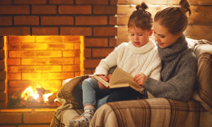 Mama s hčerko v naročju prebira pravljice ob kaminu - nevarnost CO2 so preprečili v hiši z ustreznim zračenjem.