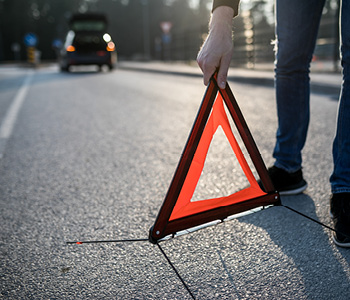 Voznik zaradi prometne nesreče postavlja varnostni trikotnik kot opozorilo drugim voznikom.