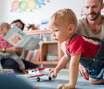 Uvajanje v vrtec – malček se v očetovi družbi igra v vrtčevskimi igračami.