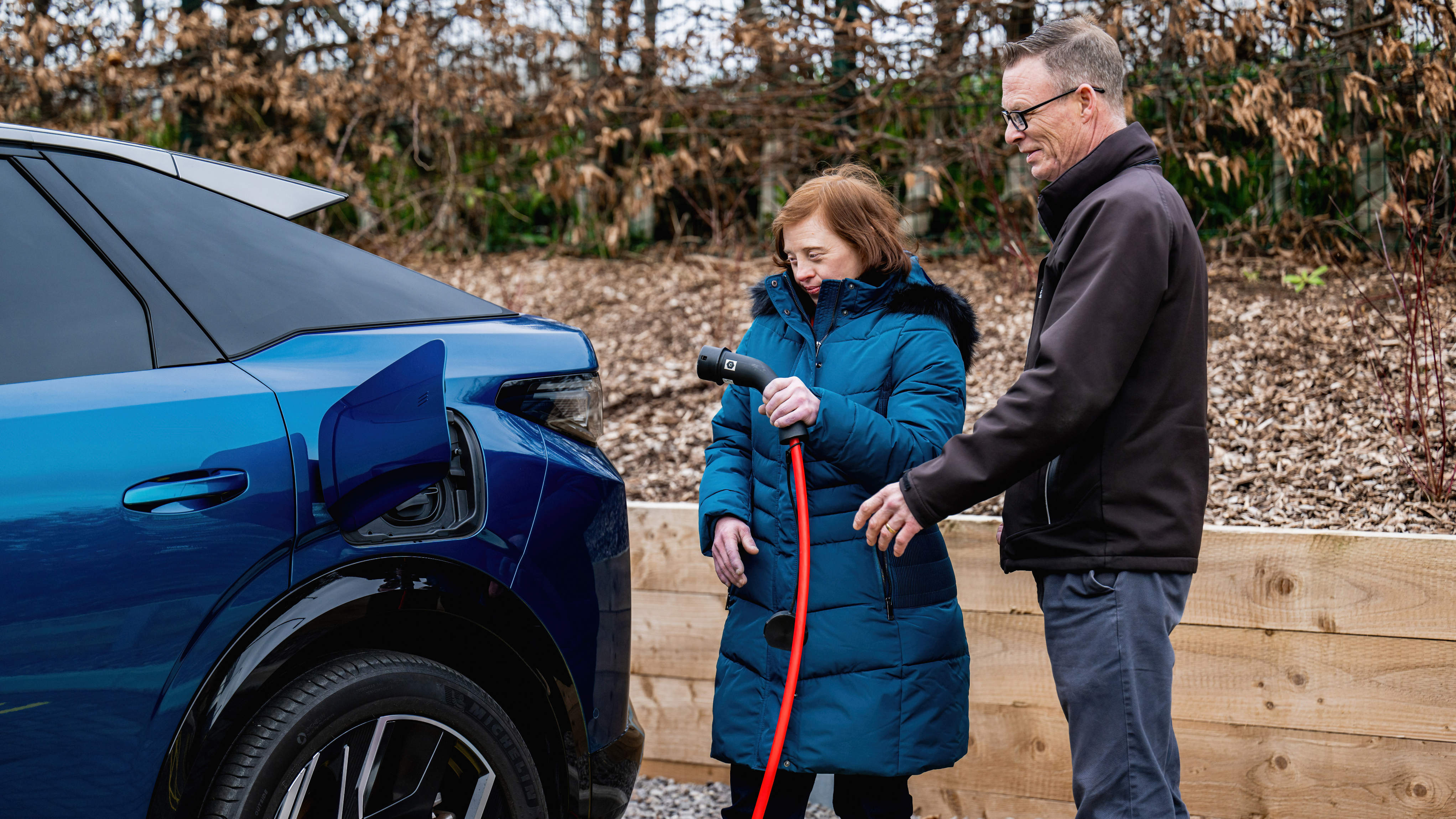 A Motability Scheme customer is placing a charger into an electric vehicle, with the guidance of a dealer.