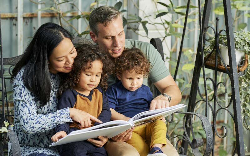 A mom and dad read a picture book to two small children.