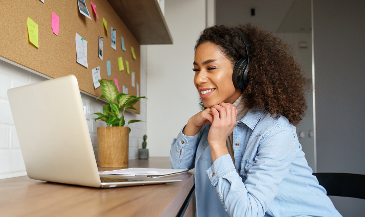 Woman with headphones smiling while studying online on her laptop