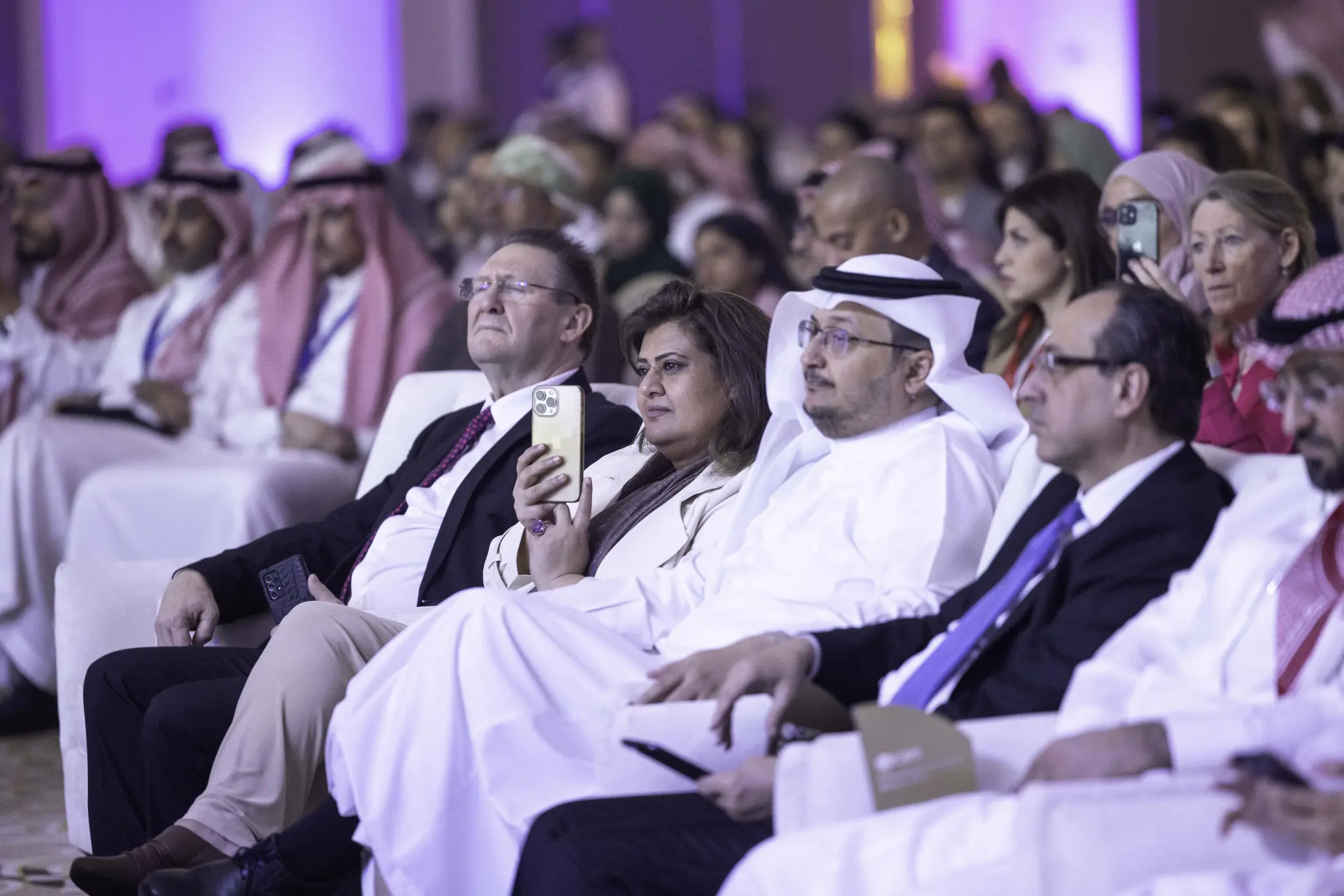 Audience members seated at a CIPS conference, some taking photos and recording on phones.