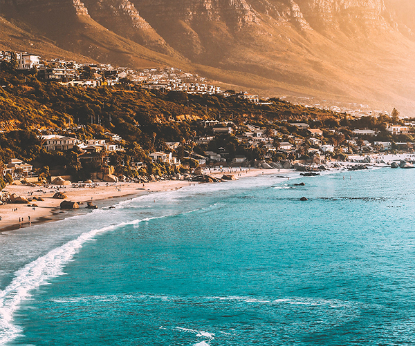 Scenic view of Camps Bay coastline in Cape Town, South Africa, with turquoise water and mountains at sunset.