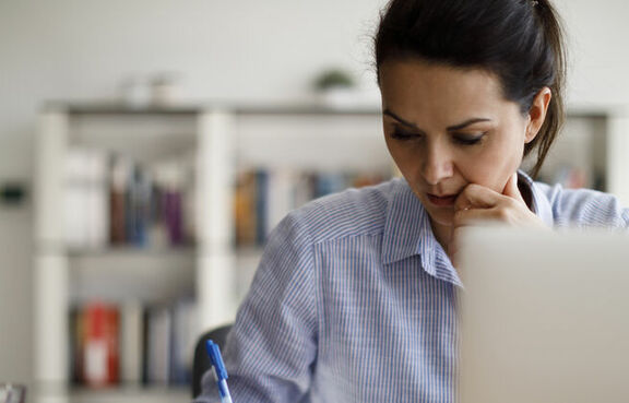 Woman writing in notepad with laptop on desk