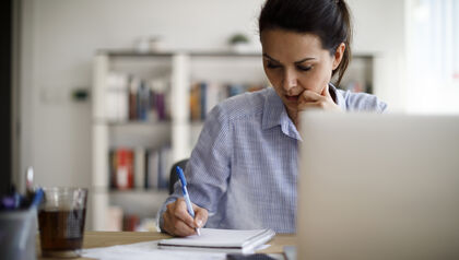 Woman writing in notepad with laptop on desk