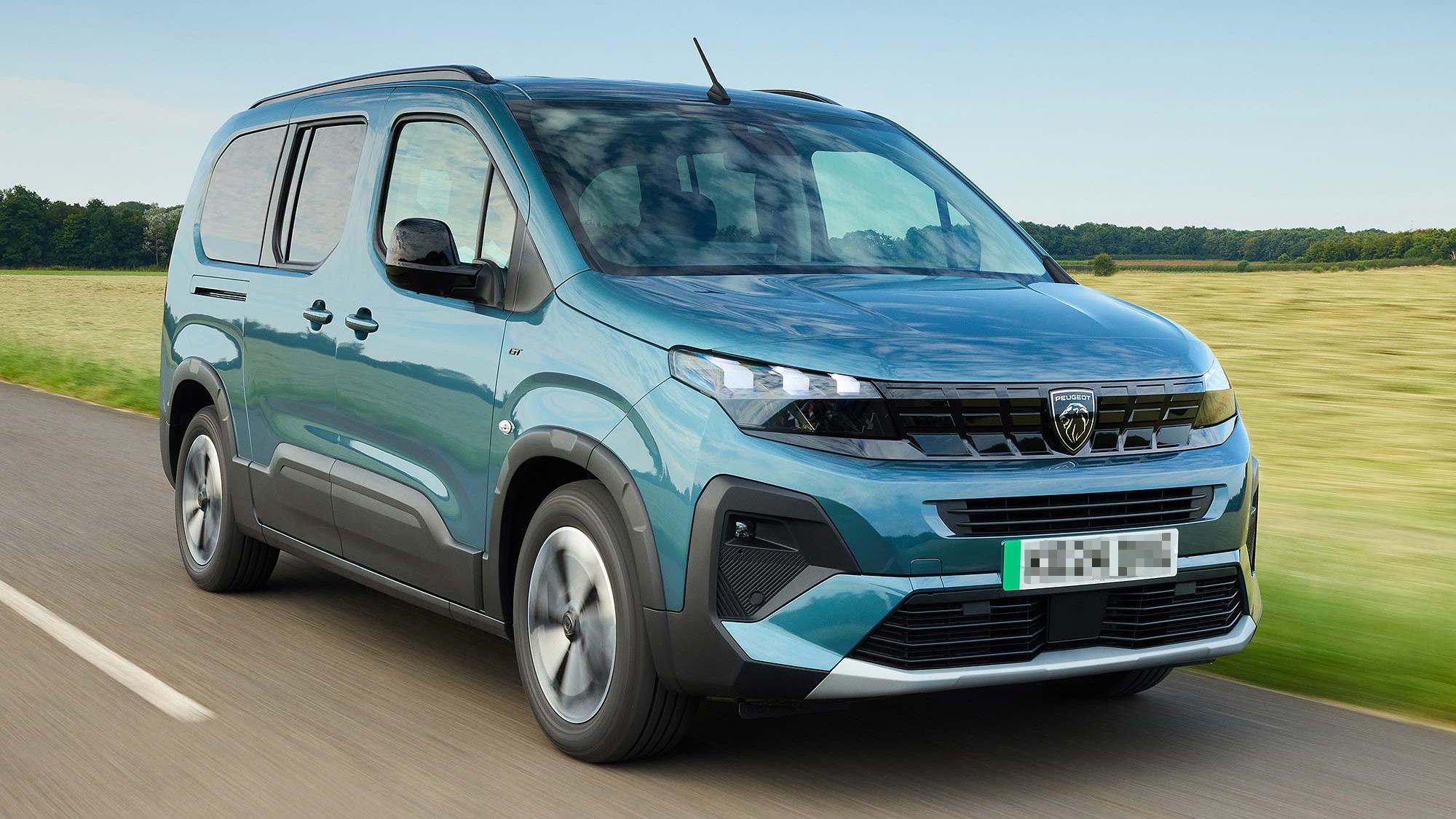 Blue Peugeot Rifter van driving along a country road, with green fields and trees in the background.