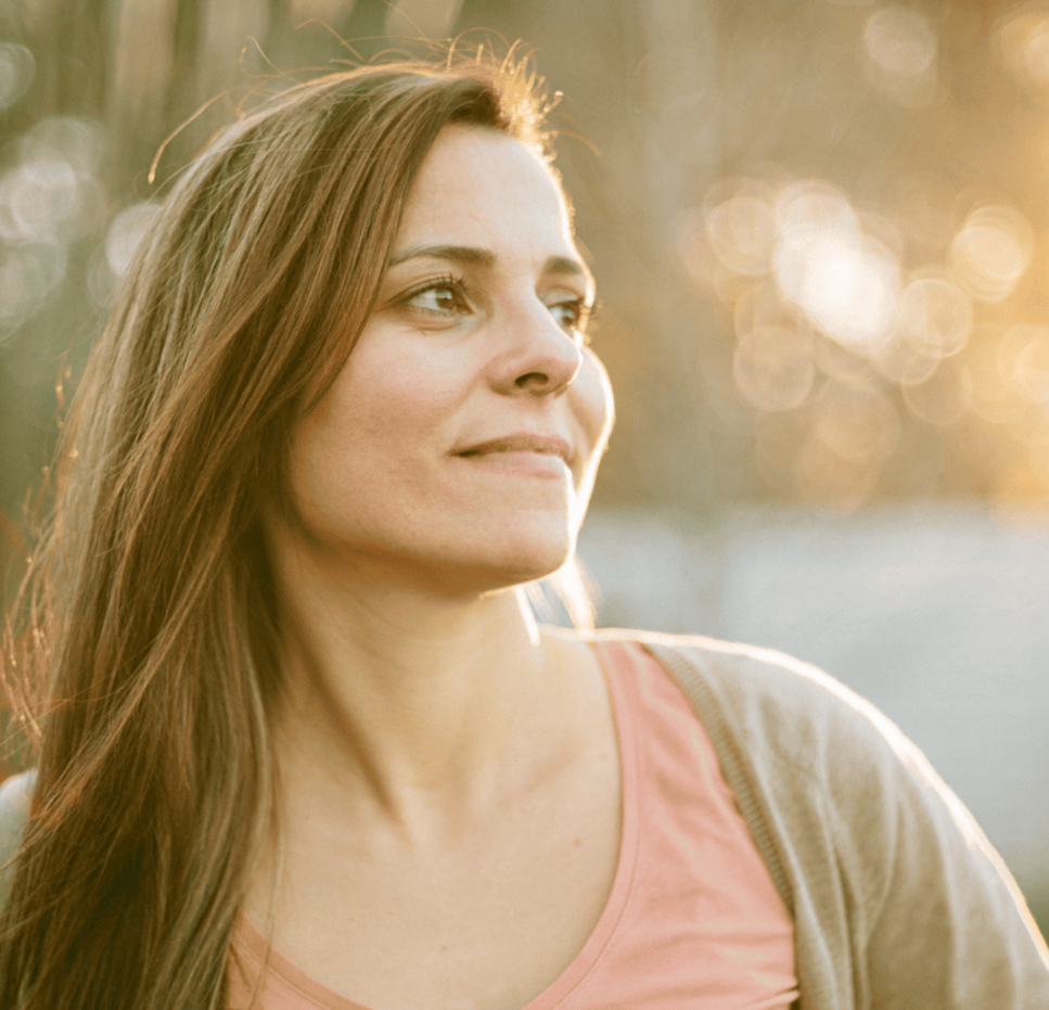 A woman stands outdoors in warm sunlight, looking hopeful and confident about the future.