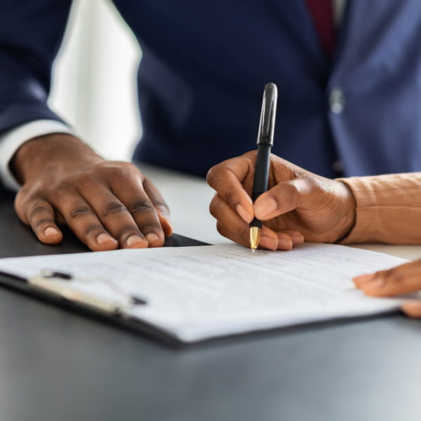 black woman in a suit signs documents sitting on a table 