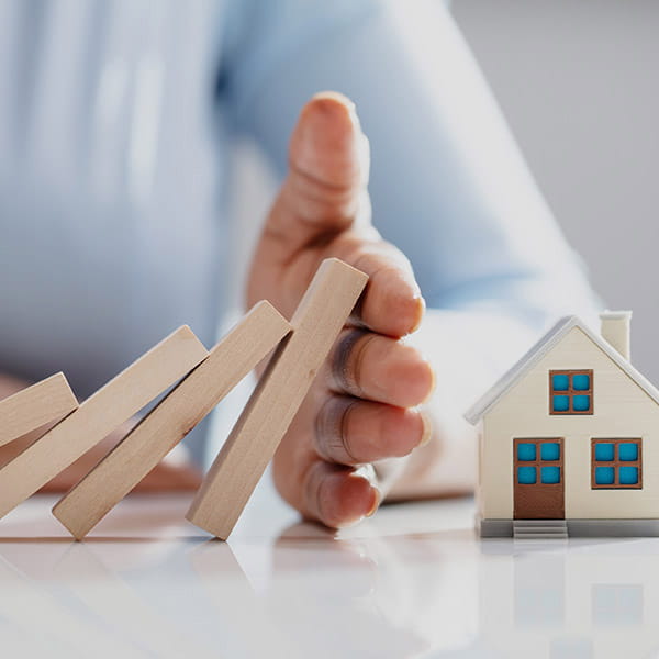 hand preventing dominos hitting a house model