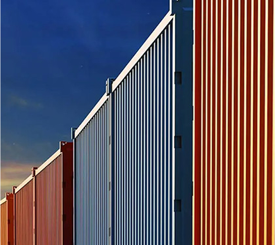 A low-angle view of a long row of colorful, vertically aligned shipping containers (supply chain theme) under a blue and orange sky.
