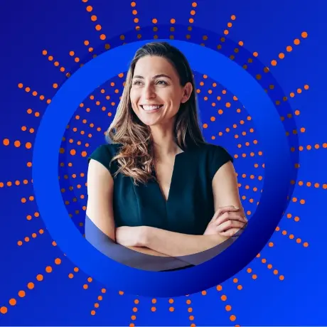 Smiling woman with long brown hair in professional attire, arms crossed, framed by a prominent blue ring on a blue background with radiating orange dot patterns
