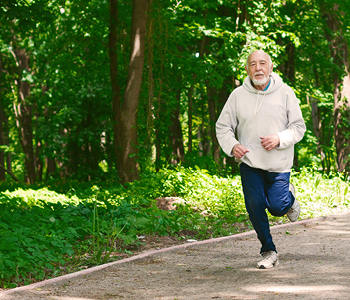 Starejši moški v trenirki teče skozi park.