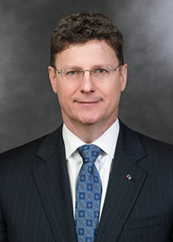 Headshot of Thom Duffy, who smiles while wearing a black suit and a blue tie