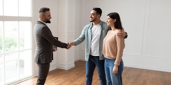 A housing professional shakes hands with a smiling couple inside their home