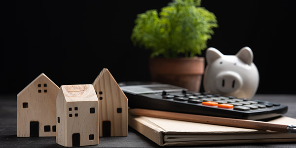 A piggy bank, calculator, and several small models of houses sit on a table